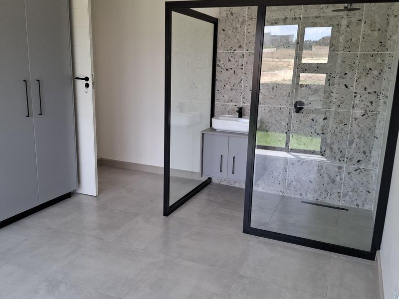 Modern bedroom featuring an open-plan en-suite bathroom with a glass shower enclosure, vanity unit, and contemporary grey floor tiling.