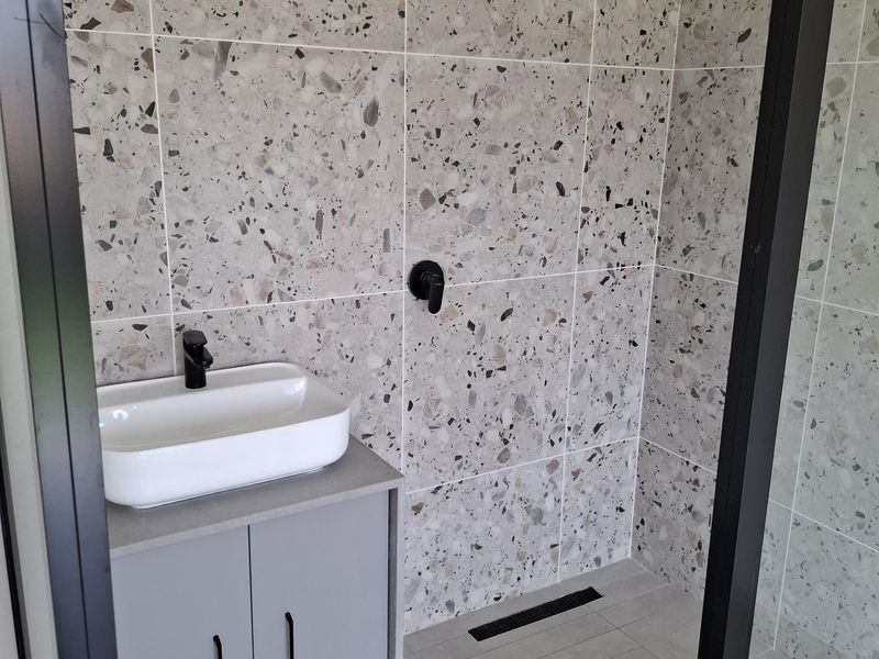 Modern bathroom featuring a walk-in shower with terrazzo wall tiles, a sleek vanity with vessel sink, and contemporary black fixtures.
