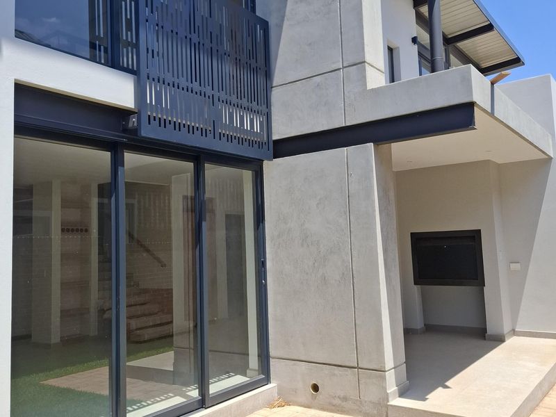 Modern rear exterior featuring a paved patio, built-in fireplace, large sliding glass doors, and contemporary concrete architectural detailing.