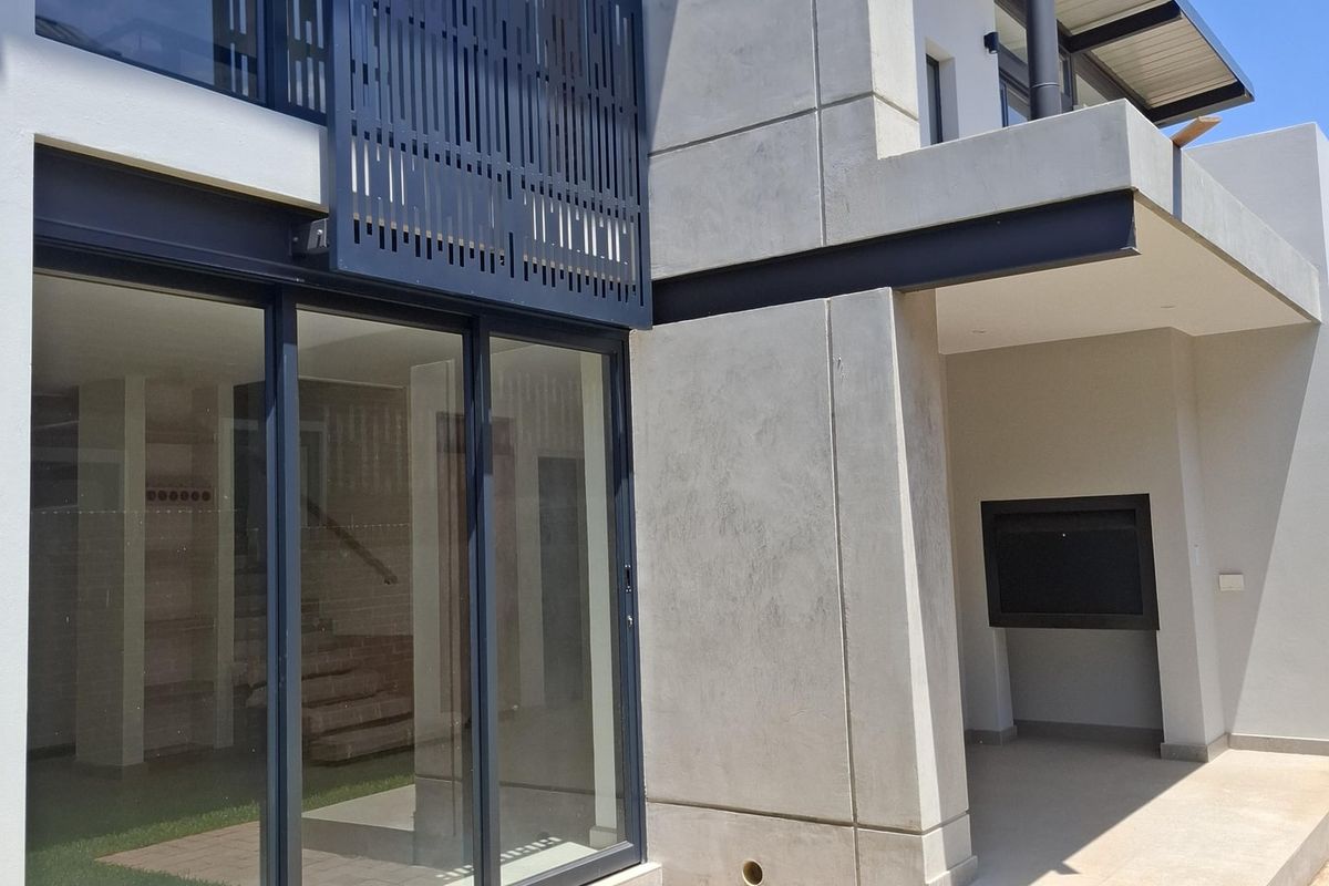 Modern rear exterior featuring a paved patio, built-in fireplace, large sliding glass doors, and contemporary concrete architectural detailing.