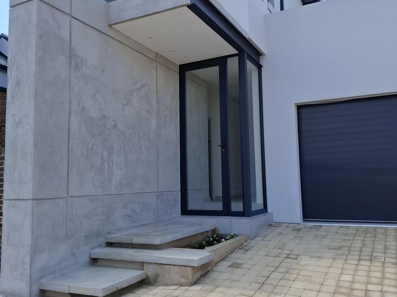 Modern front facade featuring a concrete feature wall, paved driveway, sectional garage door, and a glass entrance with integrated concrete steps.