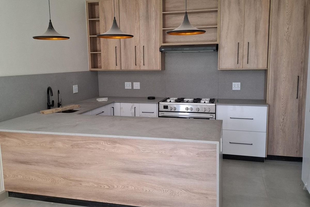 Modern kitchen featuring light wood-grain cabinetry, white lower cabinets, stone countertops, a gas stove with extractor, and a functional island with pendant lighting.