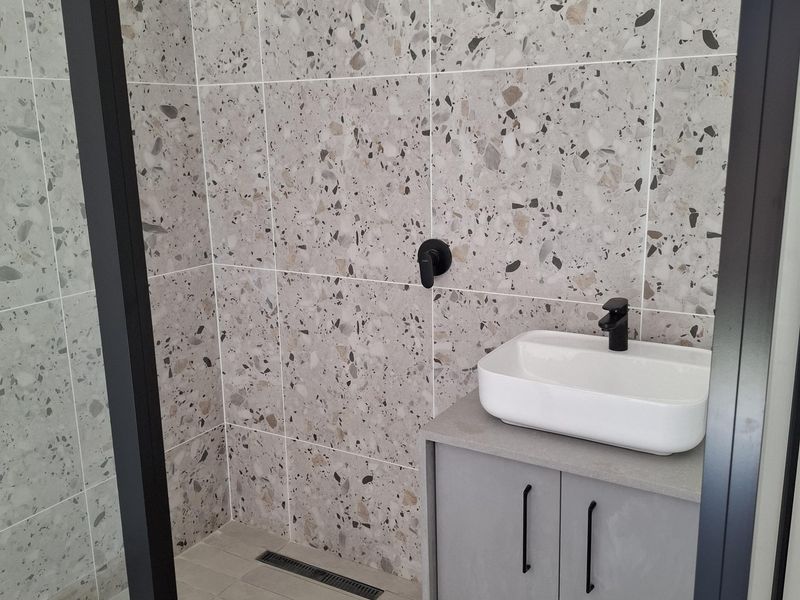 Modern bathroom featuring terrazzo wall tiles, a sleek vessel sink on a vanity cabinet, and a black rainfall shower with a glass screen.