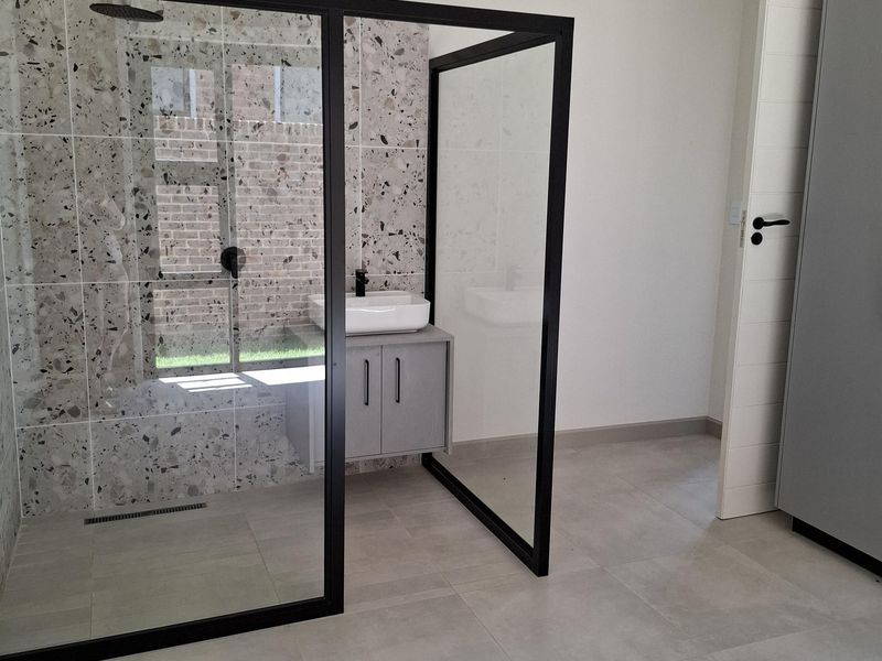 Modern bathroom featuring a walk-in shower with terrazzo tiling, a floating vanity with vessel sink, and neutral floor tiles.
