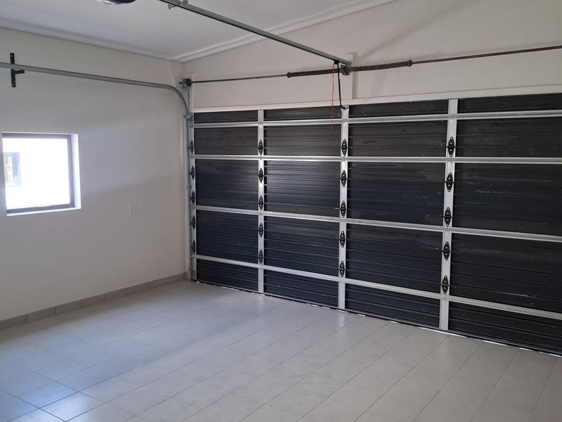 A clean, empty garage featuring tiled flooring, a sectional garage door with an automatic opener, and functional overhead lighting.