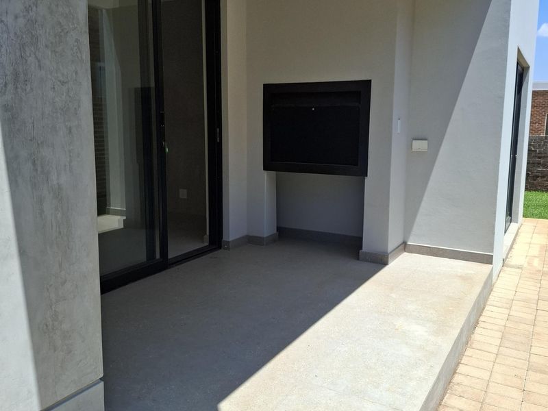 A modern covered patio featuring a built-in braai, large sliding glass doors, and clean tiled flooring, perfect for outdoor entertaining.