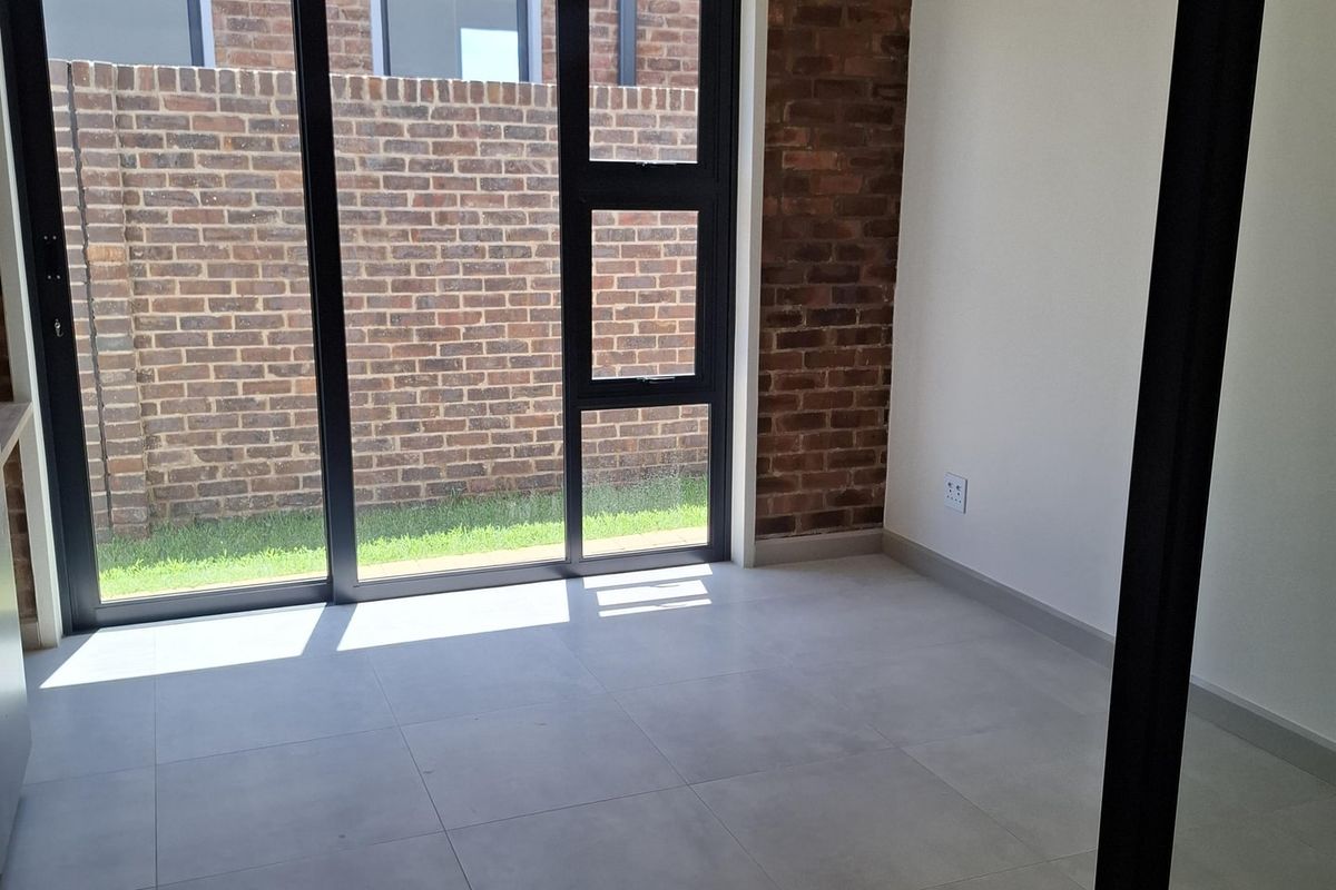A bright, modern living space featuring an exposed brick wall, large sliding glass doors leading to the exterior, and neutral tiled flooring.
