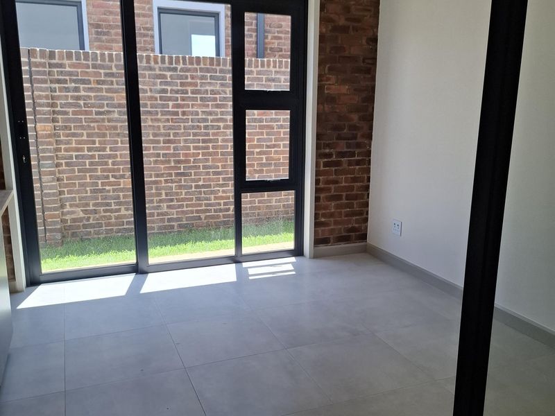 A bright, modern living space featuring an exposed brick wall, large sliding glass doors leading to the exterior, and neutral tiled flooring.