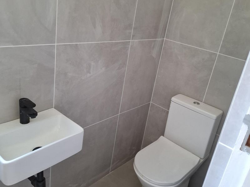 A modern, minimalist guest bathroom featuring large format grey wall tiles, a wall-mounted basin with a black mixer tap, and a white toilet.
