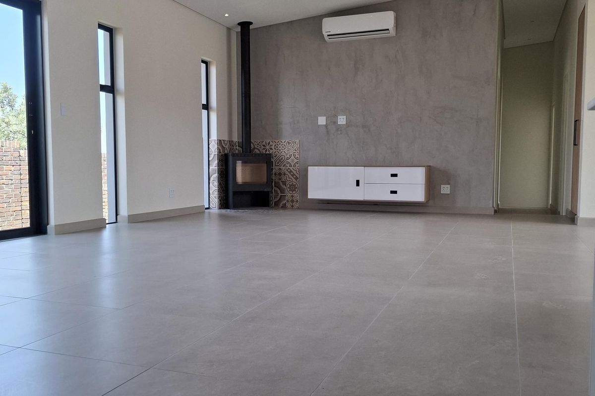 Spacious, modern living area featuring large windows, tiled floors, a built-in wood-burning fireplace, and a wall-mounted air conditioning unit.