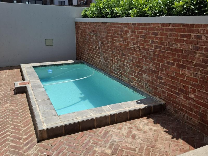 A compact swimming pool set within a private courtyard featuring herringbone brick paving and a brick boundary wall with established hedging.