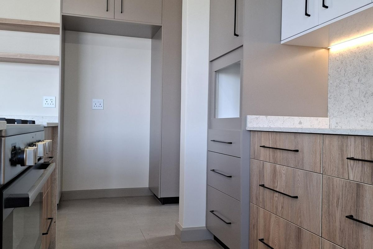 Modern kitchen featuring sleek two-tone cabinetry, stone countertops, integrated oven, and under-cabinet lighting with neutral tiled flooring.