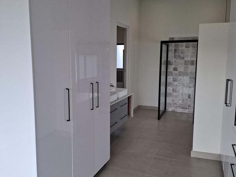 Modern bathroom featuring high-gloss built-in cabinetry, a double vanity, and a walk-in shower with contemporary tiled finishes.