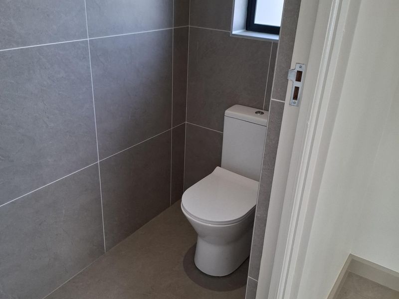 A modern, minimalist guest toilet featuring neutral grey floor-to-ceiling tiling and a clean, contemporary finish.