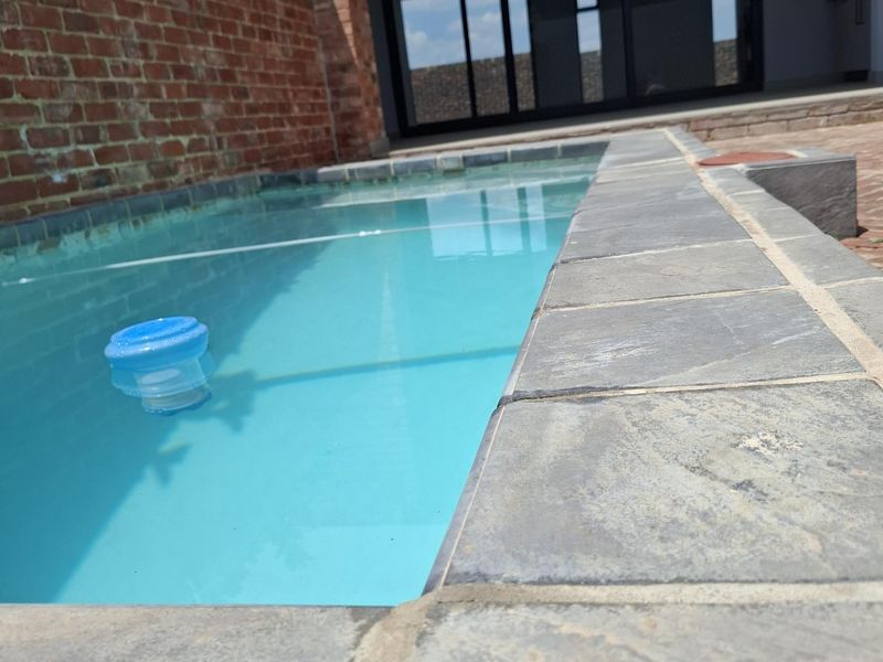 A clean swimming pool with stone coping, adjacent to a brick feature wall and modern sliding glass doors leading into the home.