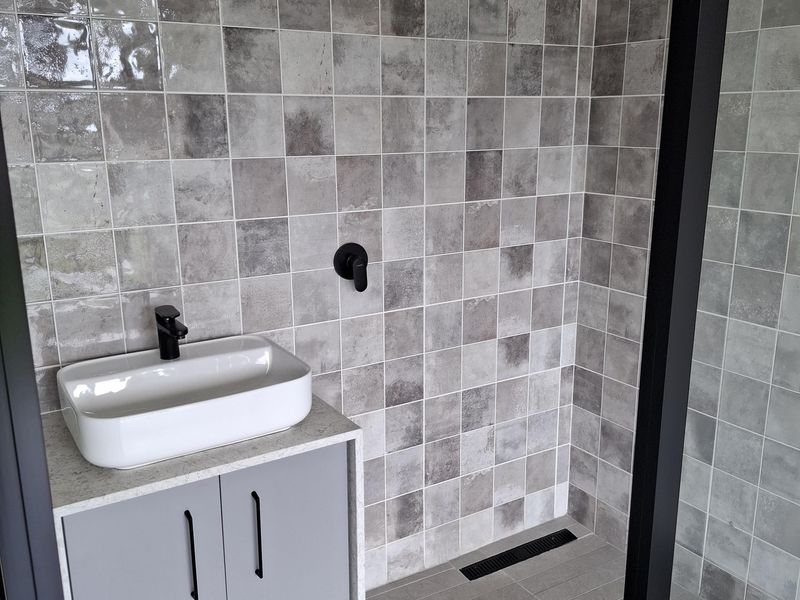Modern bathroom featuring a grey vanity with vessel sink, walk-in shower with black fixtures, and contemporary grey tiled finishes.