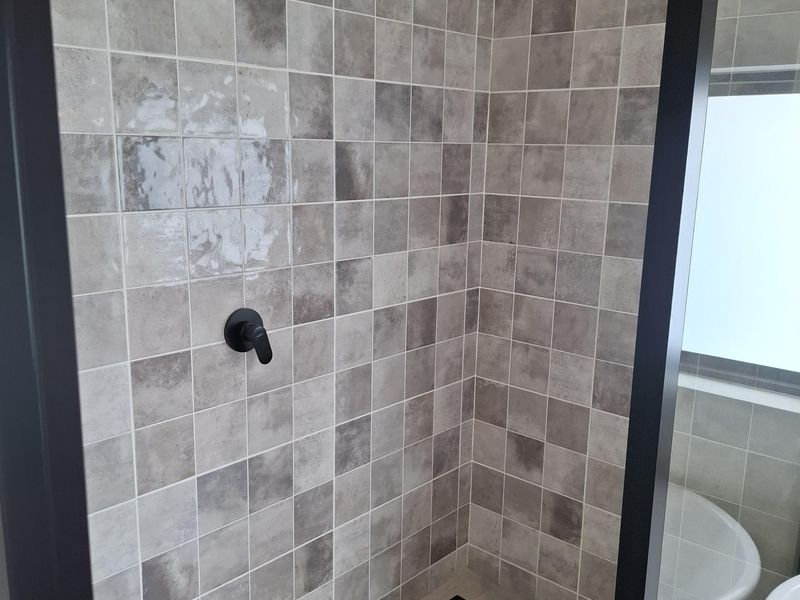 Modern walk-in shower featuring contemporary grey tiled walls, matte black fixtures, and a sleek linear drain.