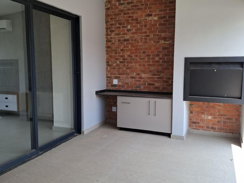Covered patio featuring an exposed brick wall, built-in braai, and sleek cabinetry, providing a modern outdoor entertainment space with seamless access to the interior.