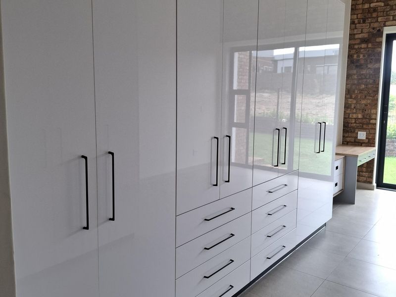 Modern bedroom featuring extensive high-gloss white built-in cupboards, an integrated desk, split-system air conditioning, and a feature exposed brick wall.
