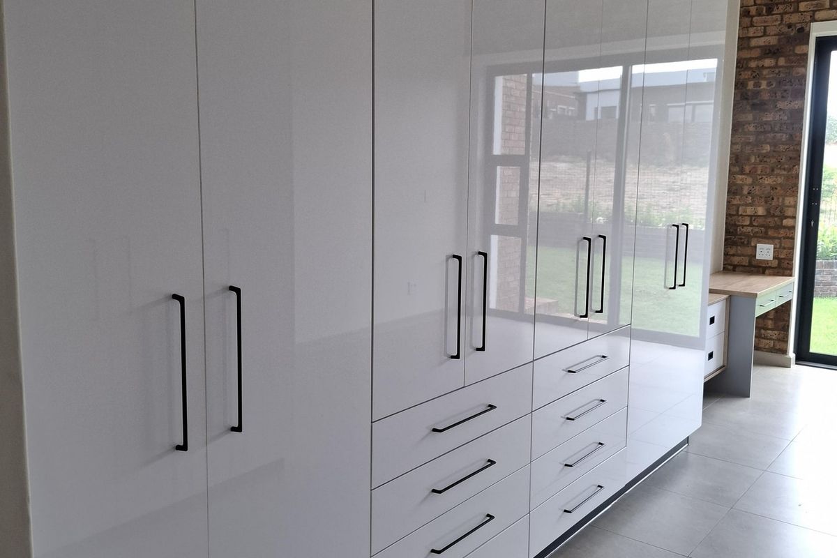 Modern bedroom featuring extensive high-gloss white built-in cupboards, an integrated desk, split-system air conditioning, and a feature exposed brick wall.