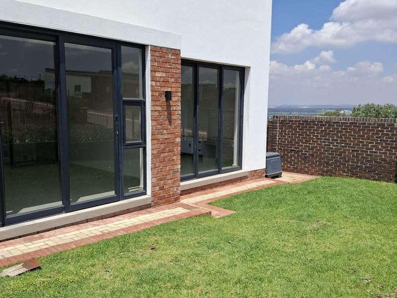 Rear view of the property featuring a modern white and brick facade, large sliding glass doors, a paved walkway, and a private garden area.