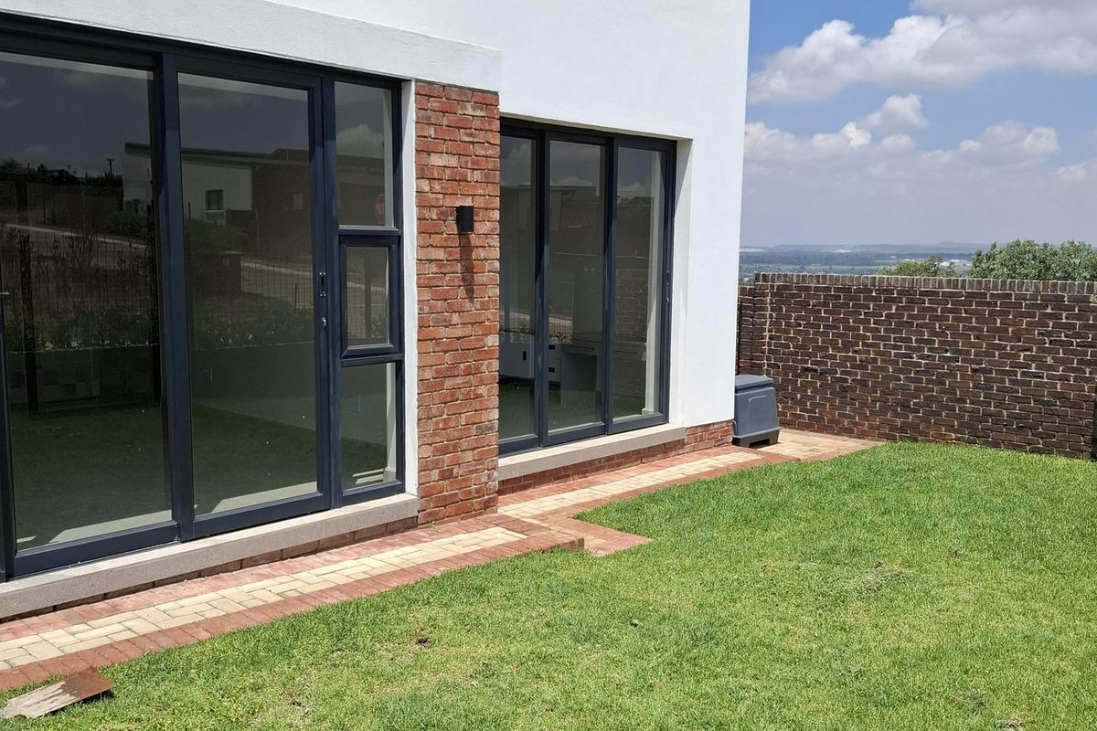 Rear view of the property featuring a modern white and brick facade, large sliding glass doors, a paved walkway, and a private garden area.