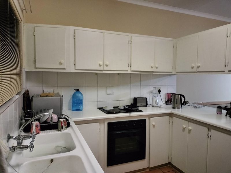 A functional kitchen featuring white cabinetry, laminate countertops, a double basin sink, and built-in oven with electric hob, finished with a tiled backsplash.