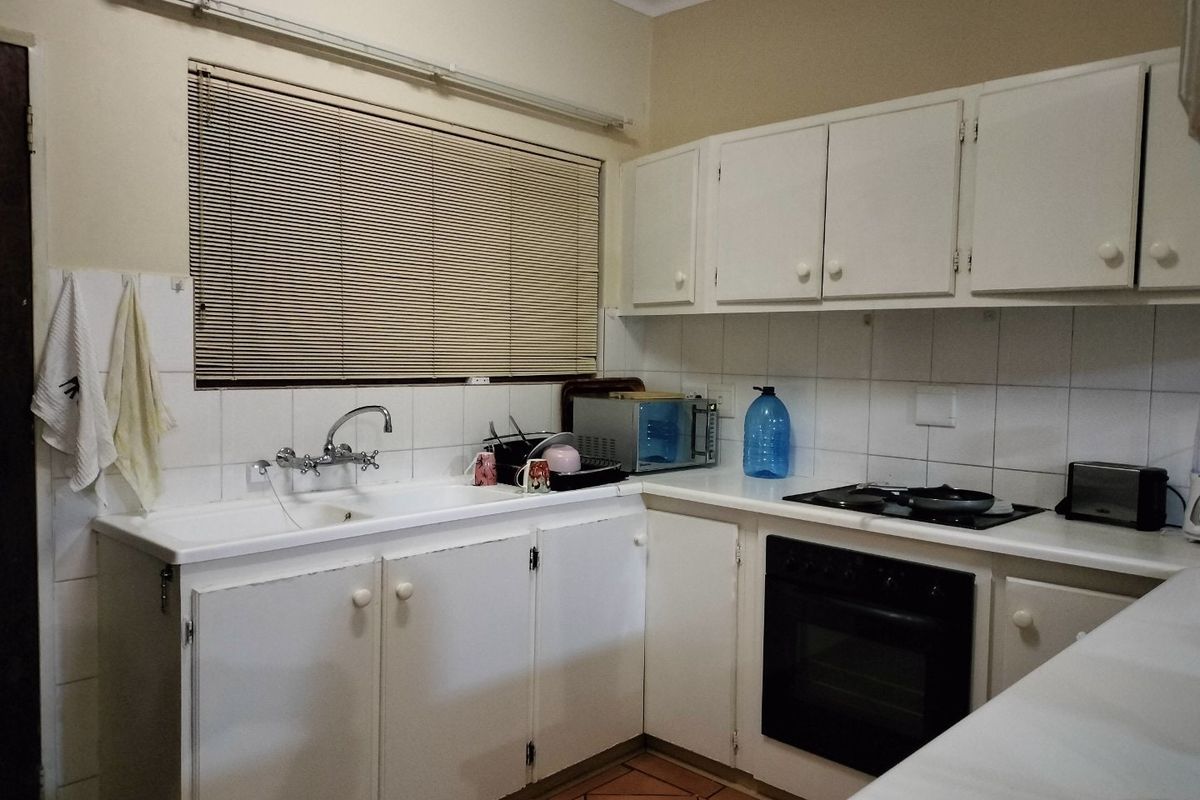 A functional kitchen featuring white built-in cabinetry, a double basin sink, tiled backsplash, and integrated oven with hob, offering a classic layout.