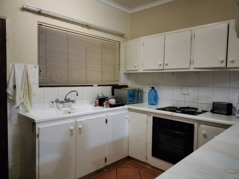 A functional kitchen featuring white built-in cabinetry, a double basin sink, tiled backsplash, and integrated oven with hob, offering a classic layout.