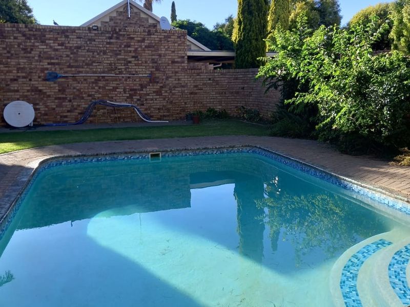 Outdoor pool area featuring a swimming pool with paved surround and a brick boundary wall.