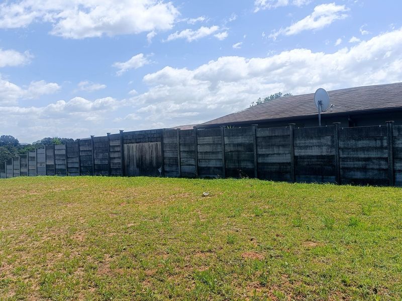 A view of a vacant residential plot featuring a weathered precast concrete boundary wall and a grassy yard area.