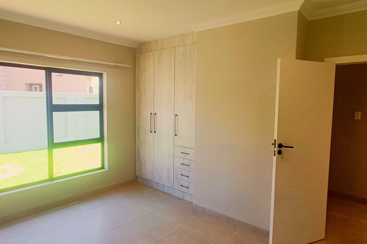 A bright, empty bedroom featuring neutral tiled flooring, built-in cupboards with a light wood finish, and modern downlighting.
