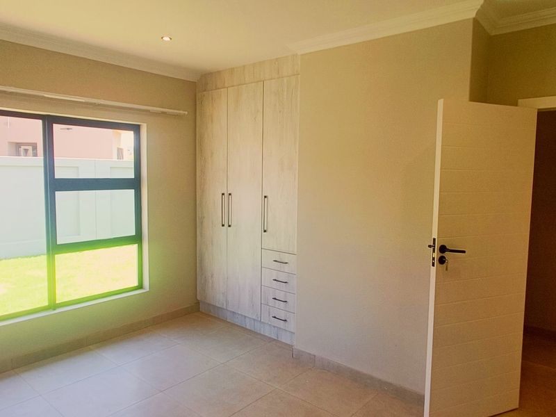 A bright, empty bedroom featuring neutral tiled flooring, built-in cupboards with a light wood finish, and modern downlighting.