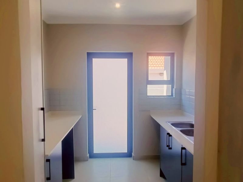 A clean, functional scullery featuring built-in cabinetry, double sink, tiled splashbacks, and direct access to the exterior.
