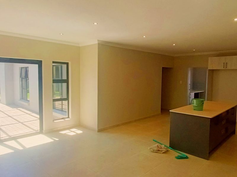 Spacious open-plan living and kitchen area featuring modern cabinetry, a central island, tiled floors, and large sliding doors opening to the patio.