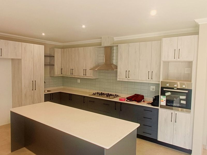 Modern kitchen featuring a central island, built-in oven, gas hob, extractor fan, and contemporary two-tone cabinetry with ample storage space.