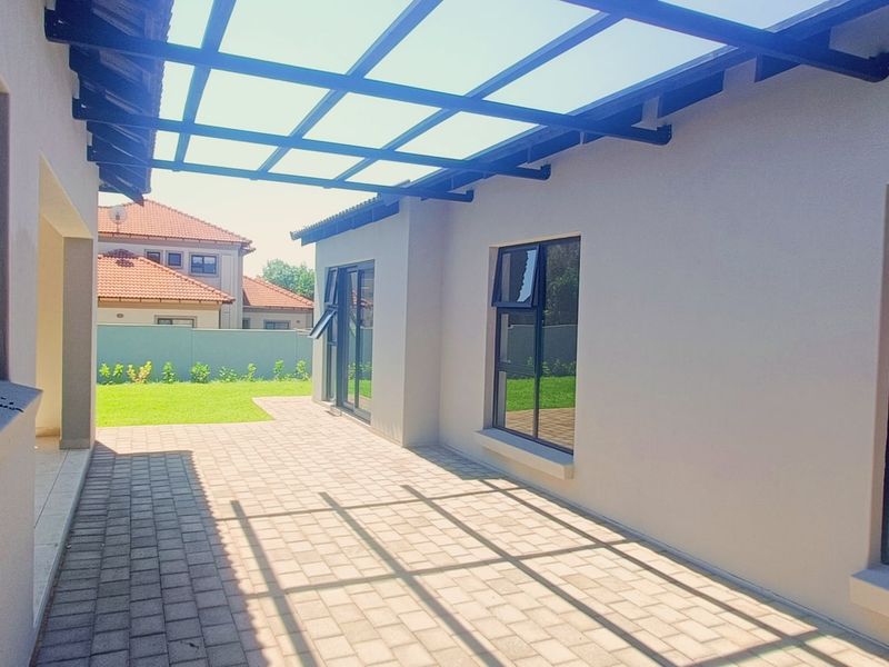 A spacious covered patio featuring paved flooring and a modern metal pergola, providing a seamless transition to the rear garden area.