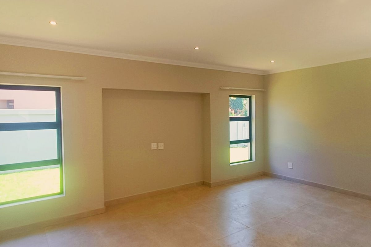 A bright and spacious living room featuring neutral walls, tiled flooring, recessed downlights, and large aluminium-framed windows.