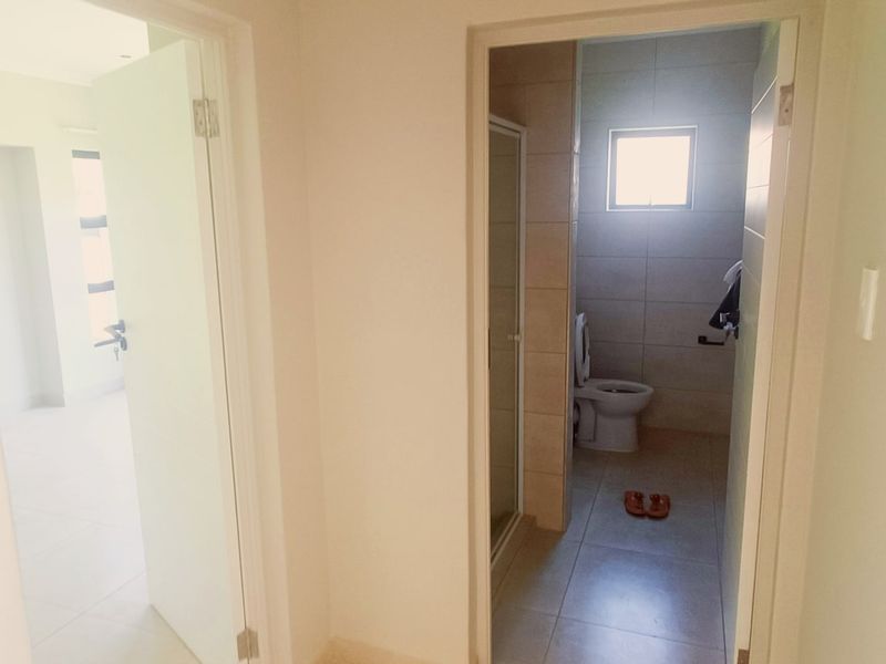 A view from a hallway looking into a bathroom and an adjacent room, featuring neutral tiled flooring and clean interior finishes.