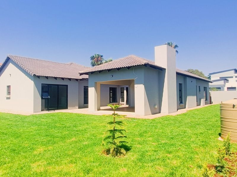 Rear view of the house featuring a covered patio, tiled roof, chimney, and a spacious lawn with a water storage tank.