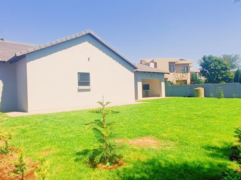 Rear view of the property featuring a well-maintained lawn, landscaped garden borders, a covered patio area, and secure boundary walls.