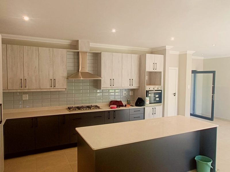 Modern open-plan kitchen featuring two-tone cabinetry, a central island, gas hob, extractor fan, and built-in oven with neutral tiled flooring.