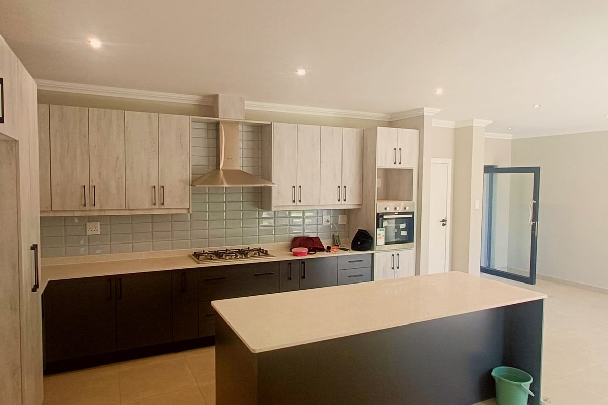 Modern open-plan kitchen featuring two-tone cabinetry, a central island, gas hob, extractor fan, and built-in oven with neutral tiled flooring.