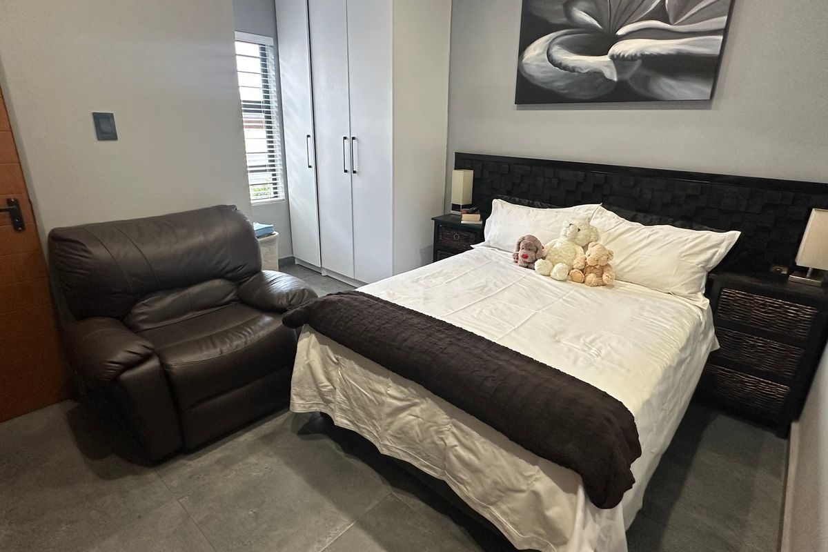 A well-maintained bedroom featuring tiled flooring, built-in cupboards, and a window with security bars.