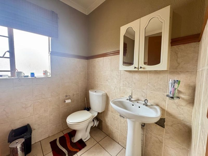 A functional bathroom featuring a pedestal basin, toilet, and wall-mounted medicine cabinet, with tiled walls and flooring throughout.