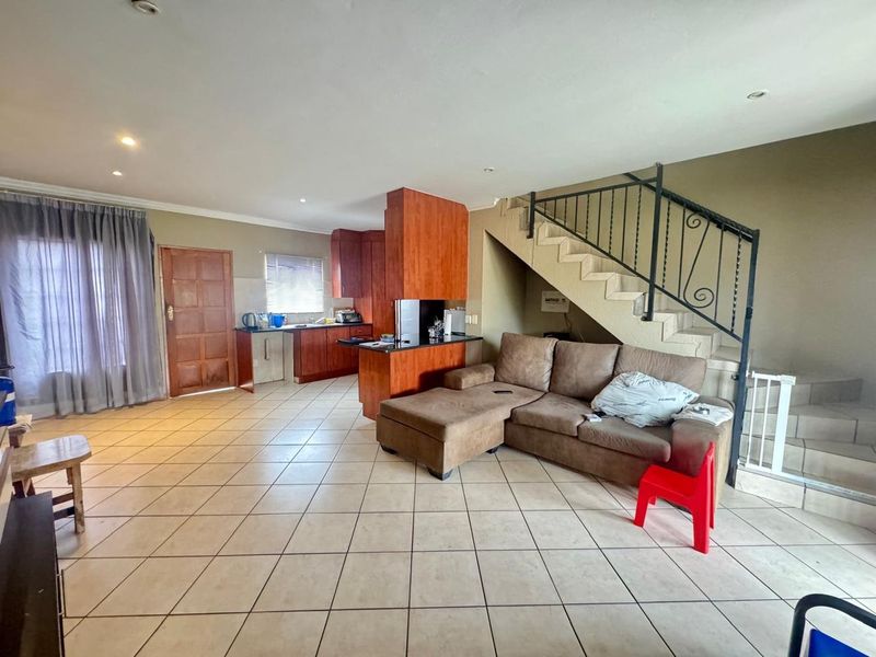 Open-plan living area featuring tiled floors, a functional kitchen with wooden cabinetry, and a staircase with a decorative wrought iron balustrade.