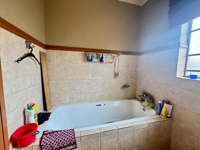 A functional bathroom featuring a built-in bathtub with tiled surround, chrome mixer tap, and handheld shower attachment.