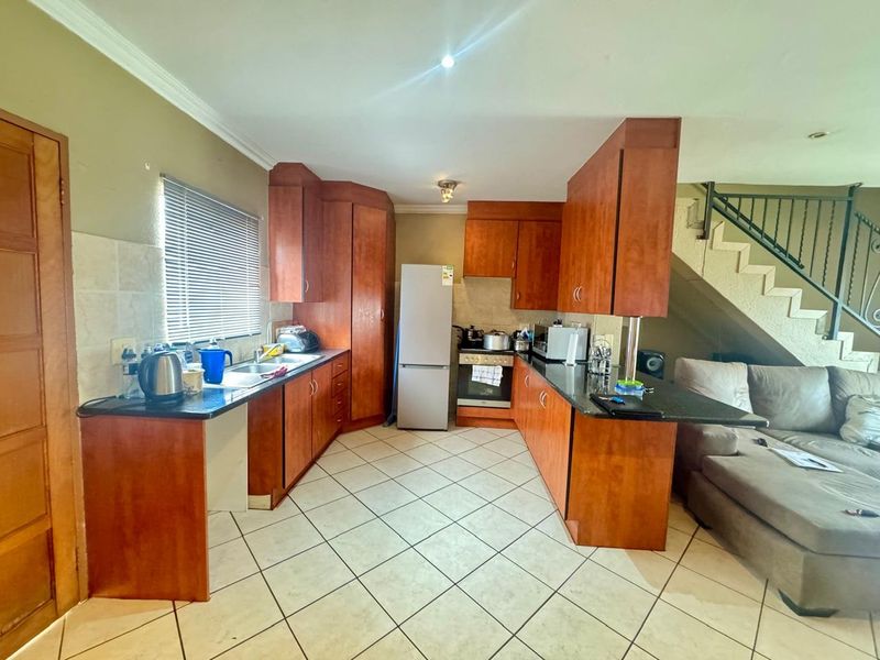 Open-plan kitchen featuring wooden cabinetry, granite countertops, and tiled flooring, seamlessly integrated with the living area and staircase access.