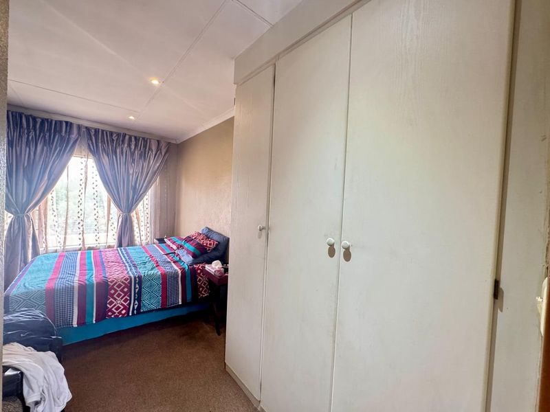 A bedroom featuring built-in cupboards, recessed downlighting, and carpeted flooring, offering a functional space with potential for cosmetic updates.