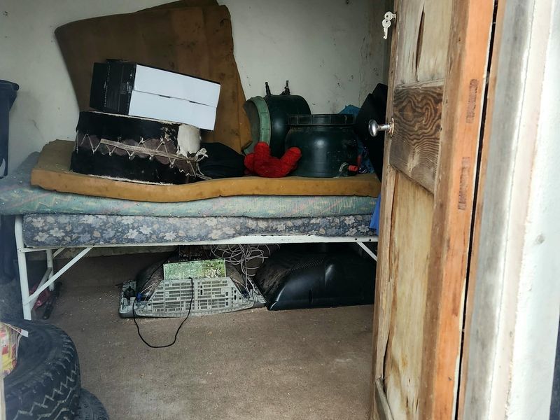A small utility or storage space featuring a concrete floor and a wooden door, currently used for miscellaneous storage.